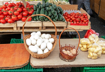 White goose eggs in rattan basket with fresh vegetables on market stall