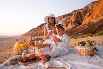 A joyful mother and son share a delightful picnic on a picturesque beach, surrounded by nature and...