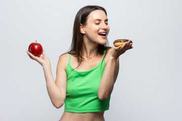 Beautiful young woman having to choose in between a donut and a red apple. On white background