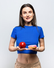 Beautiful young woman having to choose in between a donut and a red apple. On white background