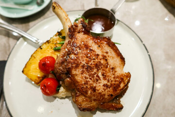 close up of pan fried grilled pork loin with bon. Pineapple and cherry tomato on the side with barbecue sauce on a big white plate with copy space