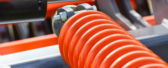 Hard orange spring made of steel. Part and detail of industrial or agricultural machine