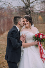 A bride and groom are hugging and kissing each other. The bride is wearing a white dress and a red ribbon