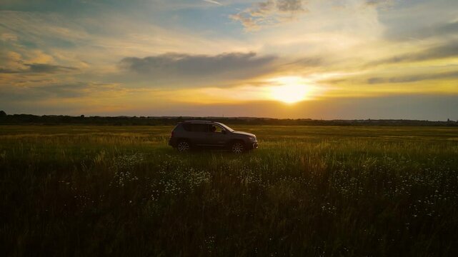 Mighty SUV driving across endless farmlands. 4x4 off road car in sunset horizon. Rural road trip summer travel escapade