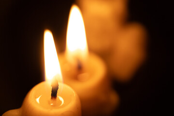 Two lit candles glow with soft, flickering flames against a dark background. The wax has melted slightly, creating a warm and peaceful glow. The image captures a peaceful.