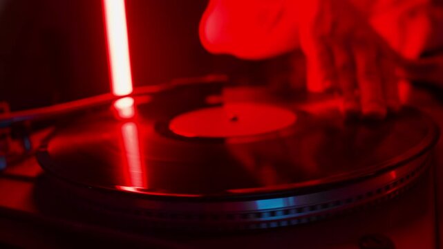 Close-up shot of hand of unknown disc jockey scratching vinyl record on turntable while playing music in night club