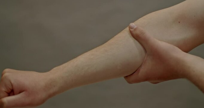 Close up shot of a man's arm as he massages his bicep and triceps muscles.