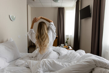 Woman stretching in bed with breakfast tray nearby
