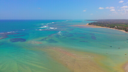Peaceful view of Jarapatinga Beach, Alagoas, with calm green and blue waters, surrounded by lush vegetation and golden sand beaches in Brazil.