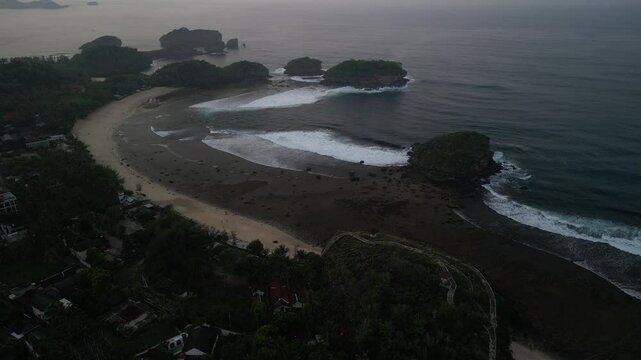 4k video footage - Aerial view of Watu Karung Beach, Pacitan, East Java, Indonesia with crashing waves during cloudy day. Cape with cliffs by the sea and green plants around at tropical island
