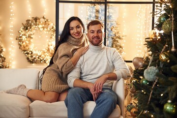 Obraz premium Sitting and smiling. Couple is celebrating new year indoors together