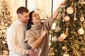 Side view, decorating the tree. Couple is celebrating new year indoors together