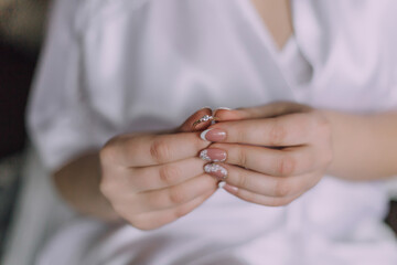 A woman is holding a ring in her hand. The ring is silver and has a diamond on it. The woman is wearing a white robe, and the image has a blurry quality to it. Scene is somewhat mysterious