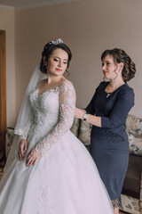 A woman in a wedding dress is getting her hair done by a woman in a blue dress. The bride is...