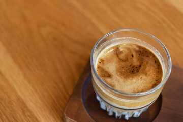 Dirty coffee on a wooden table; layered drink with a distinct robust espresso layer on the top and chilled cold milk or cream at the bottom.