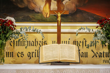 A church altar featuring an open Bible, a wooden crucifix, and floral arrangements on either side....