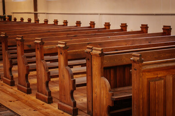 Rows of beautifully crafted wooden pews inside a church, illuminated by warm, natural light. The polished wood grain and intricate details reflect a classic, timeless design