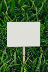 A blank sign on a wooden stake surrounded by lush green grass, ideal for text overlay or as a customizable template for various messages.