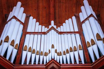 Close-up view of a grand pipe organ featuring white pipes and a polished wooden frame. The...