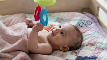 A content baby lying on their back on a soft quilt, looking up at a colorful hanging mobile, with a hint of a smile on their face.