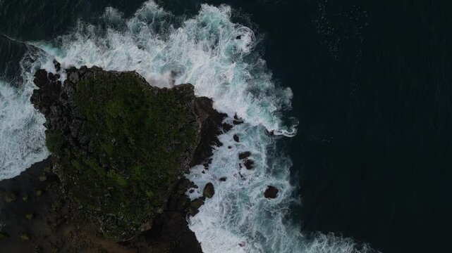 4k video footage - Aerial view of Watu Karung Beach, Pacitan, East Java, Indonesia with crashing waves during cloudy day. Cape with cliffs by the sea and green plants around at tropical island