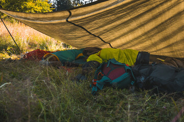 Cozy camping setup under a tarp in the wilderness, featuring sleeping bags and backpacks. A rustic...