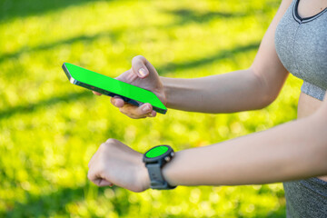 Close-up of Asian woman using smartphone and smartwatch for fitness tracking in outdoor park