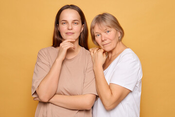 Two women pose together against a bright yellow backdrop, showcasing a moment of connection in a studio setting, captured in daylight for a warm atmosphere
