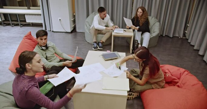 Group of students working together on a project in geometry class after normal classes. They sit on bean bag chairs around a table, helping each other to understand the math problems and learn.