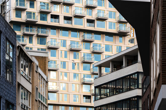 This image showcases a modern architectural complex, featuring numerous blue balconies reflecting the sunlight, with an urban background adding depth and dimension in Rotterdam