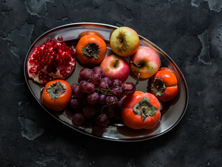 Seasonal fruits - persimmon, red grapes, apples, pomegranate on a dark background, top view