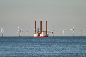 Jack up wind turbines installation vessel in the sea, with wind turbines farm on the background.