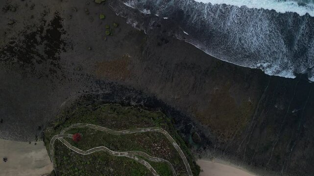 4k video footage - Aerial view of Watu Karung Beach, Pacitan, East Java, Indonesia with crashing waves during cloudy day. Cape with cliffs by the sea and green plants around at tropical island