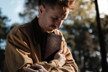 Fototapeta premium Christian read and pray with holy bible in forest with Holy light shining. Pray to God to confess your sins and ask for blessings to overcome his problems. faith, and religion.