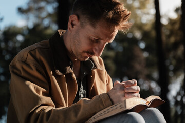 Christian read and pray with holy bible in forest with Holy light shining. Pray to God to confess your sins and ask for blessings to overcome his problems. faith, and religion.