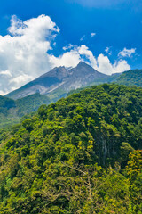 Fototapeta premium Close-up panorama of active volcano in clear daytime. Mount Merapi in Yogyakarta, Indonesia is truly enchanting when seen up close with a hill in the foreground and a cloudy blue sky in the background