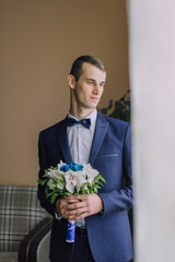 A man in a suit holding a bouquet of flowers. He is wearing a blue suit and a blue bow tie