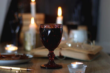 Books, lit candles, red wine, snacks and various deocration on the table. Dark academia or Halloween concept. Selective focus.