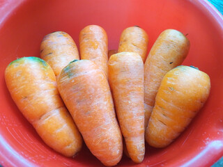Close-up of vibrant orange carrots arranged neatly in a red bowl highlighting their natural...