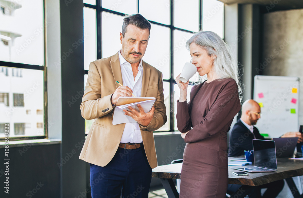 Poster two professionals engage in a discussion at a stylish office, with one taking notes while the other 