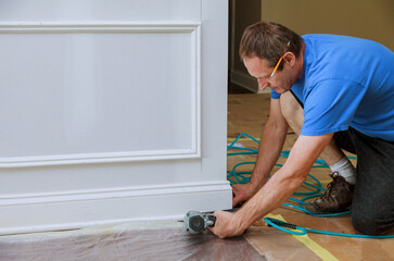 Carpenter carefully fits baseboard trim in room undergoing renovation uses power tools ensures...