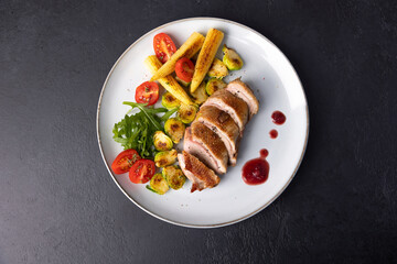 Grilled duck breast fillet with Brussels sprouts, mini corn, cherry tomatoes, arugula and lingonberry sauce. Traditional Mediterranean cuisine. Selective focus, close-up.
