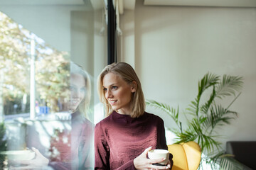 Happy woman holding coffee cup near office window