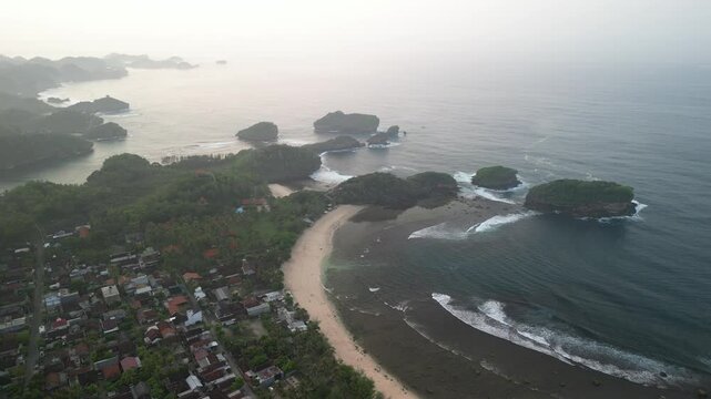 4k video footage - Aerial view of Watu Karung Beach, Pacitan, East Java, Indonesia with crashing waves during cloudy day. Cape with cliffs by the sea and green plants around at tropical island