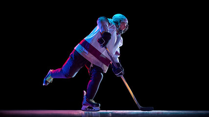 Side view dynamic image of man, hockey player in motion with stick, training, playing intense game against black studio background in neon light. Concept of sport, game, tournament, competition