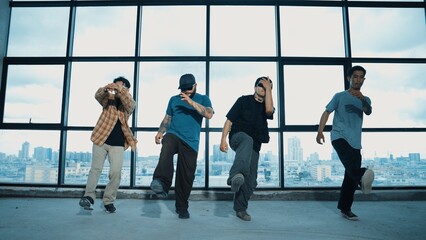Obraz premium Group of multicultural dancer dancing together with skyscraper. Portrait of multicultural hipster team moving foot step with confident near window with urban city view. Outdoor sport 2024. Hiphop.