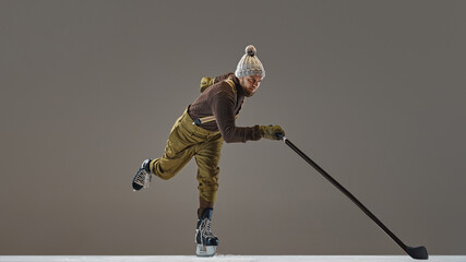 Obraz premium Winter sports. Man wearing knitted sweater, hat and pants with suspenders, ice skating with stick, playing hockey. Concept of sport, game, tournament, action, competition
