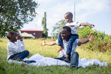 A joyful family day in the park with a cheerful father, young boy on his shoulders, and another child taking photos. A perfect depiction of happiness and togetherness in nature.