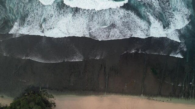 4k video footage - Aerial view of Watu Karung Beach, Pacitan, East Java, Indonesia with crashing waves during cloudy day. Cape with cliffs by the sea and green plants around at tropical island