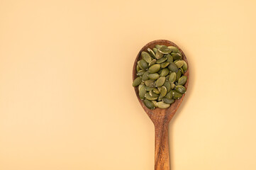 Fresh pumpkin seeds in a wooden spoon on beige background, top view flat lay. Organic eco healthy seeds, superfood, diet food, healthy vegetarian food. Green Smoothie Ingredient 